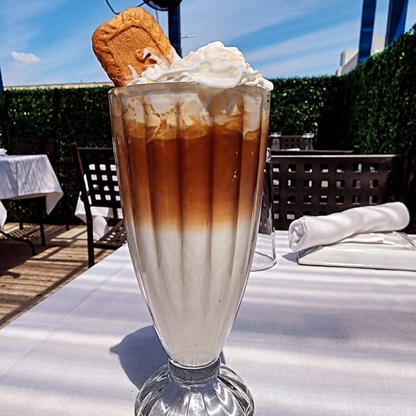 Iced coffee with whipped cream and a cookie on a white-clothed outdoor table at The Bay Cafe.