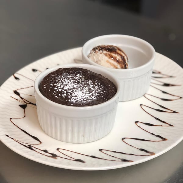 Chocolate lava cake with powdered sugar and a scoop of vanilla ice cream with chocolate syrup.