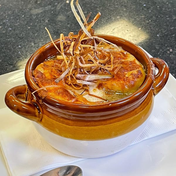 A brown and white crock of French onion soup with melted cheese and crispy fried onions.