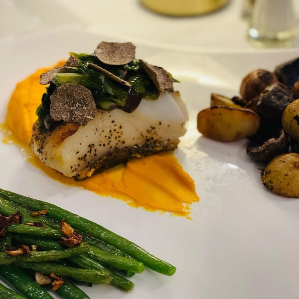 Pan-seared fish with truffle slices, green beans, roasted potatoes, and orange puree on a white plate.