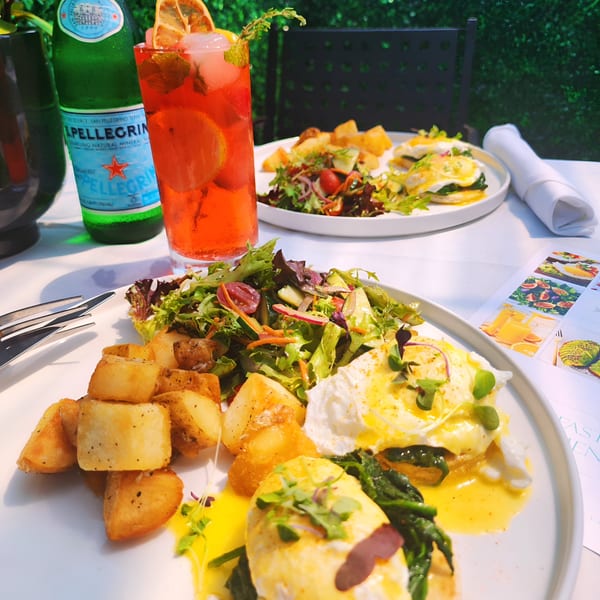Two plates of Eggs Benedict with roasted potatoes and salad, alongside drinks at The Bay Cafe.