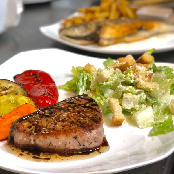 Seared tuna steak with grilled vegetables and a Caesar salad on a white plate.
