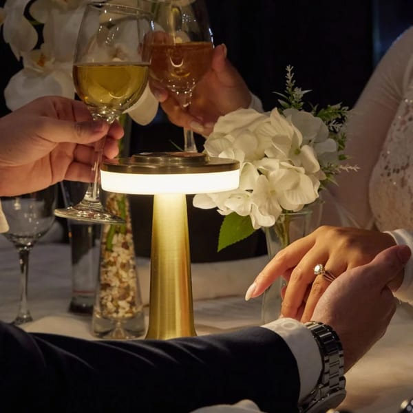 Couple holding hands and toasting wine glasses at a romantic dinner table with a glowing lamp.