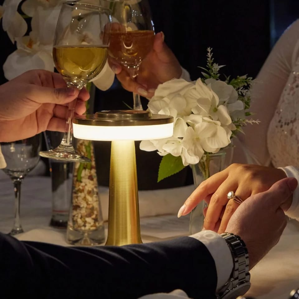 Couple holding hands and toasting wine glasses at a romantic dinner table with a glowing lamp.