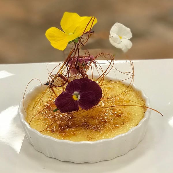 Crème brûlée in a white ramekin, garnished with spun sugar and colorful edible flowers.
